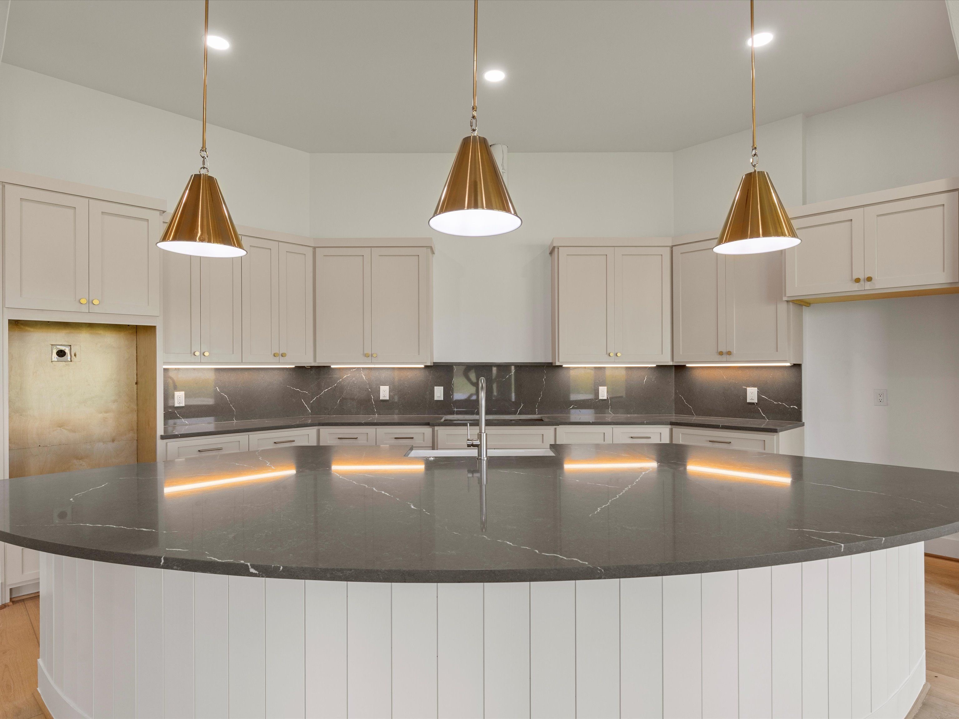 A modern kitchen featuring an island with dark stone countertop, white cabinetry, and stylish pendant lighting.