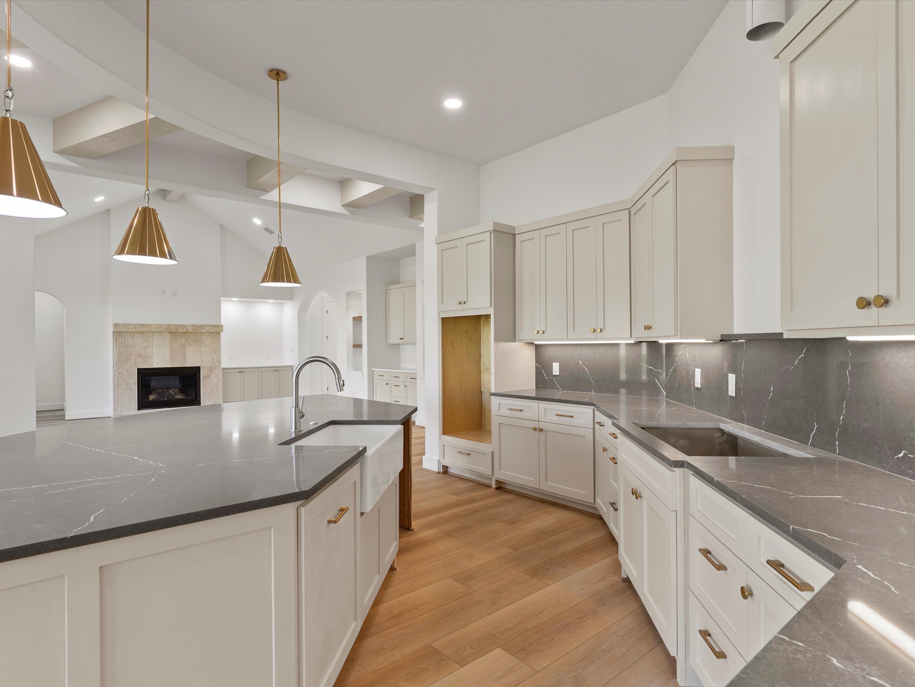 A modern kitchen featuring white cabinets, a large gray marble countertop, and stylish pendant lighting.