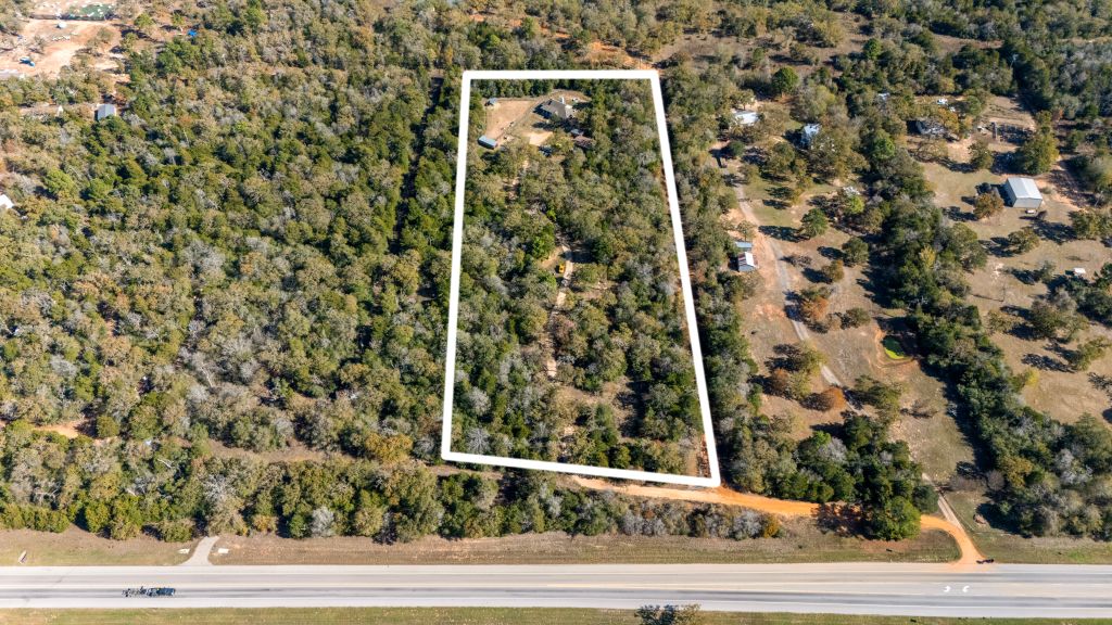 Aerial view of wooded rural land beside a paved roadway and dirt access route